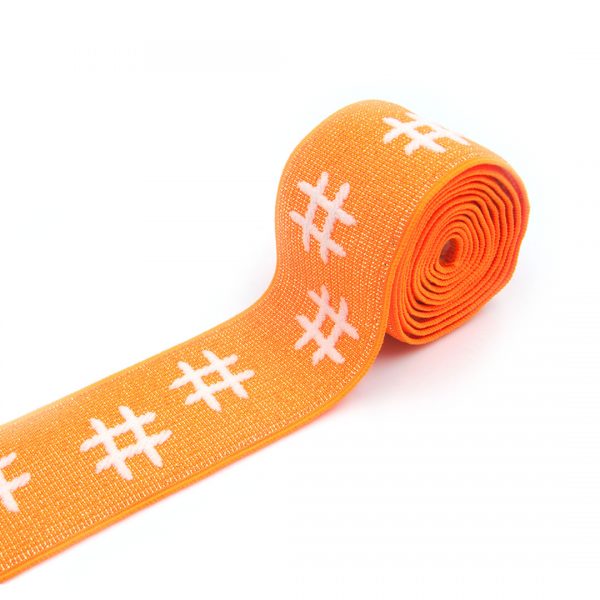 Guma tkana żakardowa w kolorze pomarańczowym z przędzą metalizowaną i białym wzorem, do odzieży sportowej.